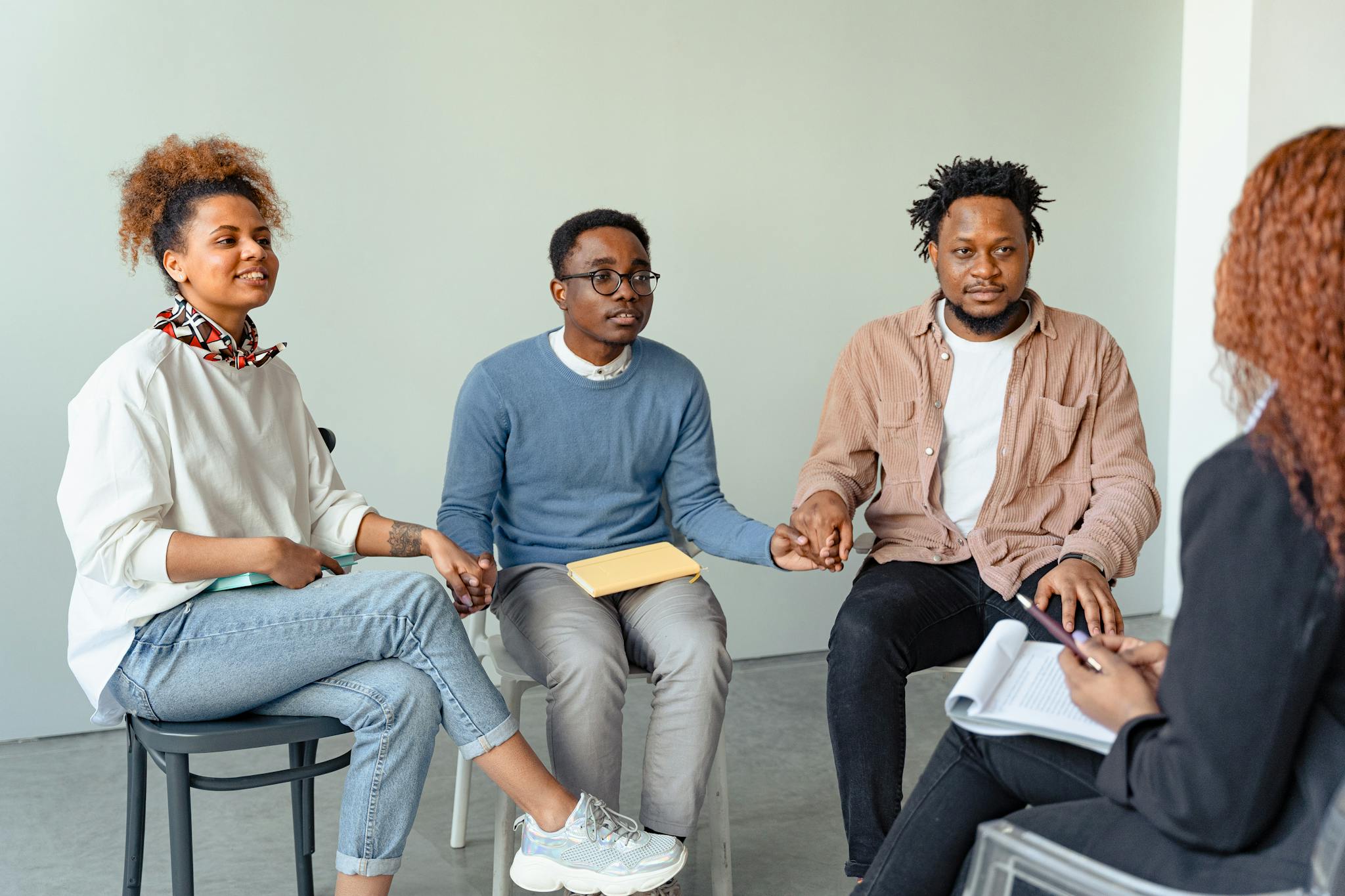 A diverse group of adults in a supportive therapy session, holding hands indoors.